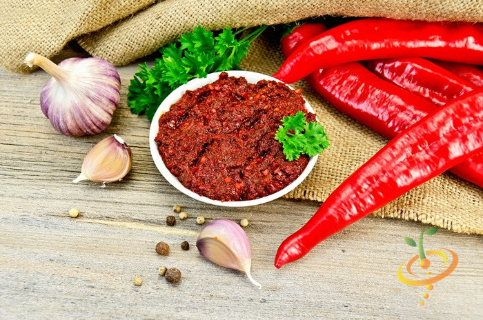 Tabasco peppers with spicy red sauce, garlic cloves, and parsley on wooden surface