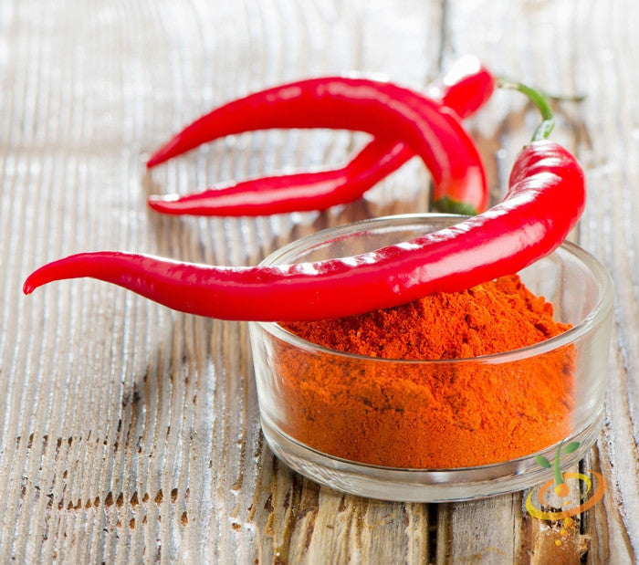 Two red cayenne peppers resting on a glass bowl filled with red cayenne pepper powder on a wooden surface