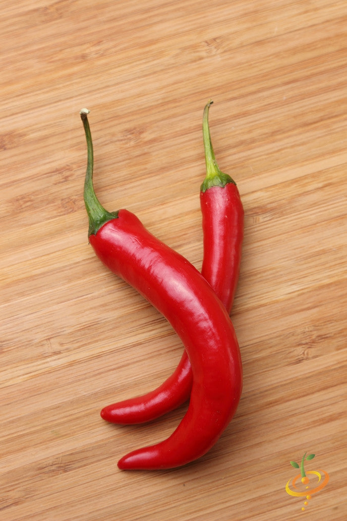 Two bright red cayenne peppers on a wooden surface