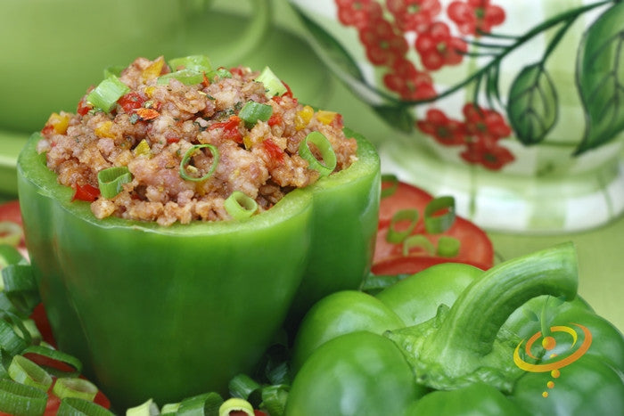 Green bell pepper stuffed with ground meat and garnished with chopped green onions next to whole green bell peppers and a decorative ceramic pitcher