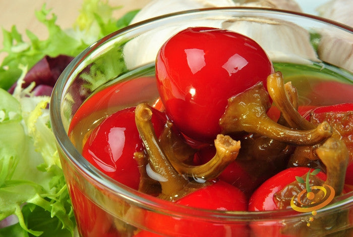 Close-up of bright red hot cherry peppers in a glass jar with leafy greens in the background